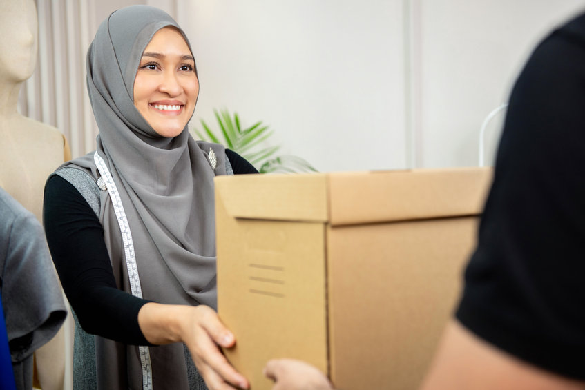 Muslim woman designer receiving parcel box from delivery man at her tailor shop